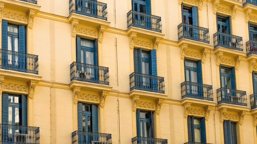 Elegant yellow building facade with intricate balcony design and blue shutters.