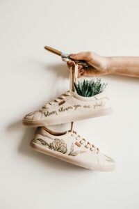 Hand holding decorated shoes with plant embroidery and creative quote design.