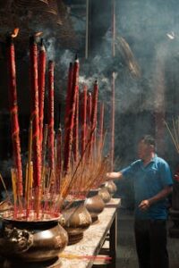 Man in traditional temple performing incense ritual with vibrant red incense sticks, enveloped in smoke.