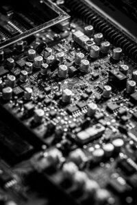 Detailed black and white close-up of an electronic circuit board with capacitors and transistors.